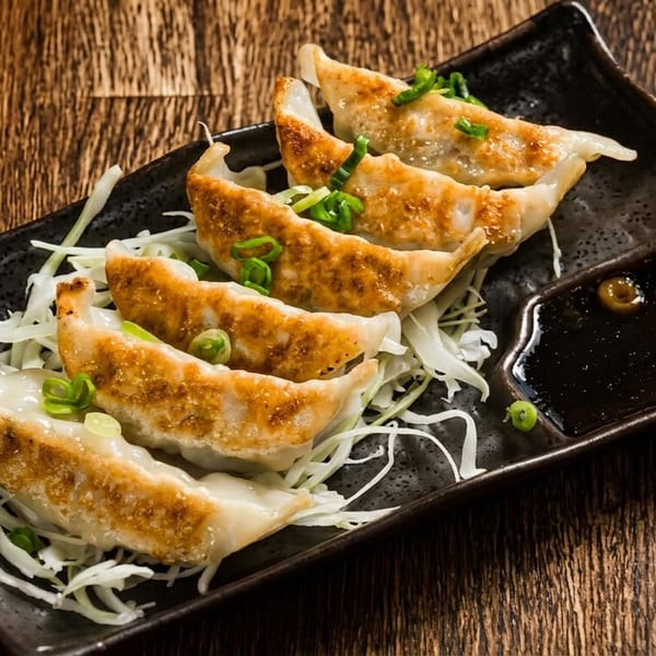 Five pan-fried gyoza dumplings with green onions and shredded cabbage, served with soy sauce.