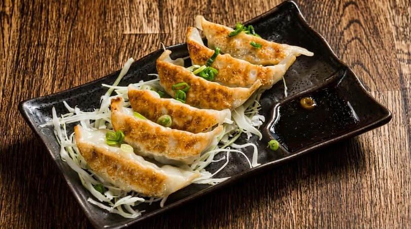 Five pan-fried gyoza dumplings with green onions and shredded cabbage, served with soy sauce.