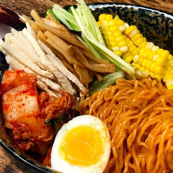 Spicy ramen bowl with noodles, kimchi, corn, egg, and vegetables on a wooden table.
