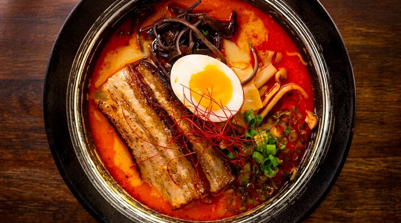 Spicy ramen bowl with pork belly, a soft-boiled egg, mushrooms, and green onions.