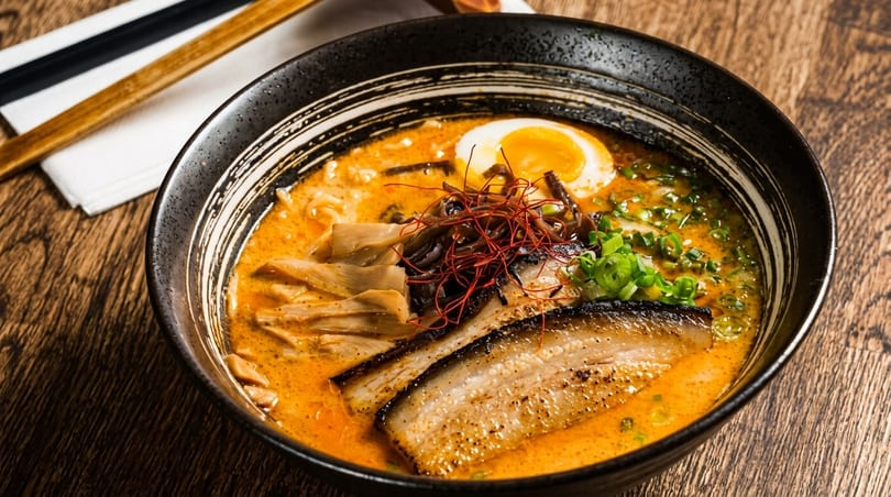 A bowl of ramen with pork belly, a soft-boiled egg, bamboo shoots, and green onions.